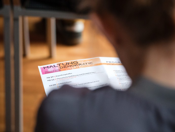 Blick über die Schulter einer Person, die das Tagungsprogramm in der Hand hält. (vergrößerte Bildansicht wird geöffnet)