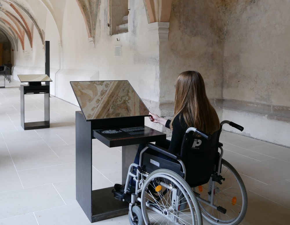 Eine Frau im Rollstuhl schaut sich über einen Spiegel die Decke im LWL-Museum Kloster Dalheim an.