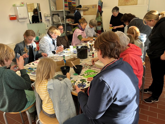 Eine Gruppe von Kindern und Erwachsenen sitzt zusammen um einen Tisch  und bastelt.