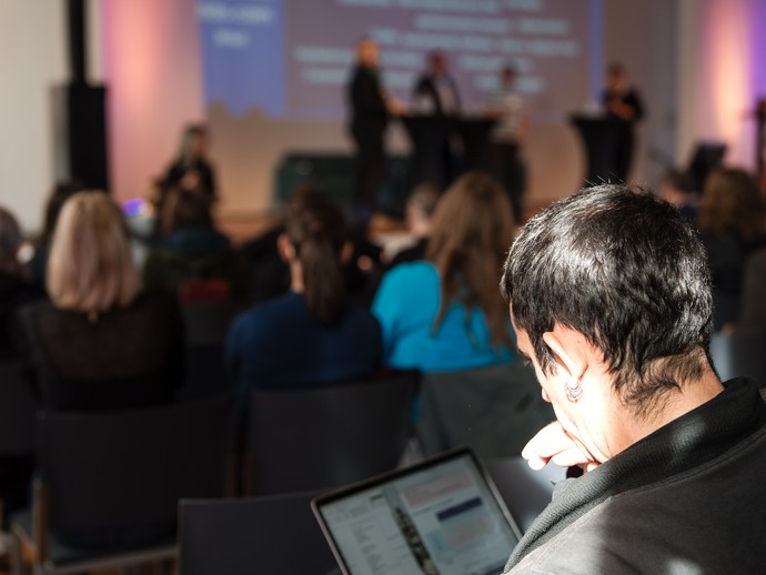 Blitzlicht zu den Foren und Person mit Laptop im Publikum. (vergrößerte Bildansicht wird geöffnet)