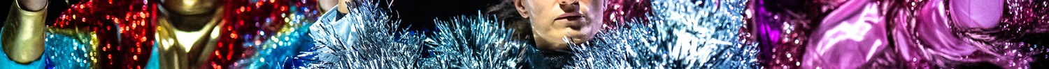 Zu sehen sind drei Personen in bunt-glitzernder Kleidung, die ihre Hände in die Luft recken.
