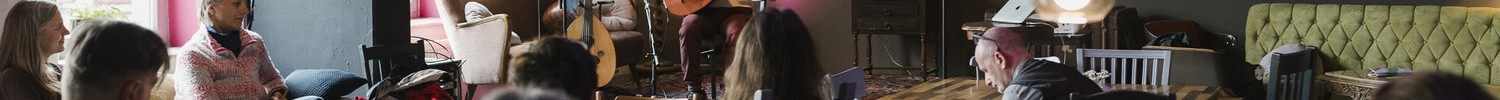Ein Mann spielt auf der Bühne ein Saiteninstrument. Verschiedene Menschen sind im Publikum zu sehen.