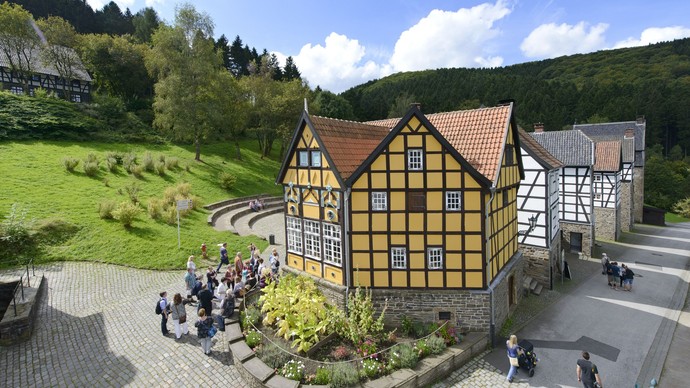 Besucher:innen vor einem gelbem Fachwerkhaus und dahinter weitere Gebäude im Freilichtmuseum.