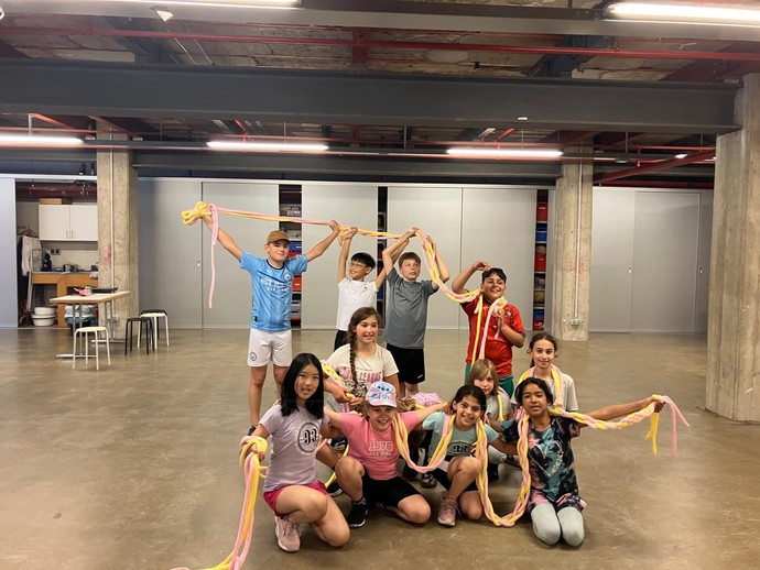 Eine Gruppe von Kindern in einer Halle, die bunte Schlingen aus Stoff halten und posieren.
