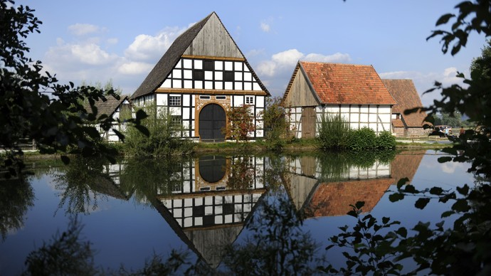 Zwei Häuser im LWL-Freilichtmuseum Detmold, die sich im Wasser spiegeln.
