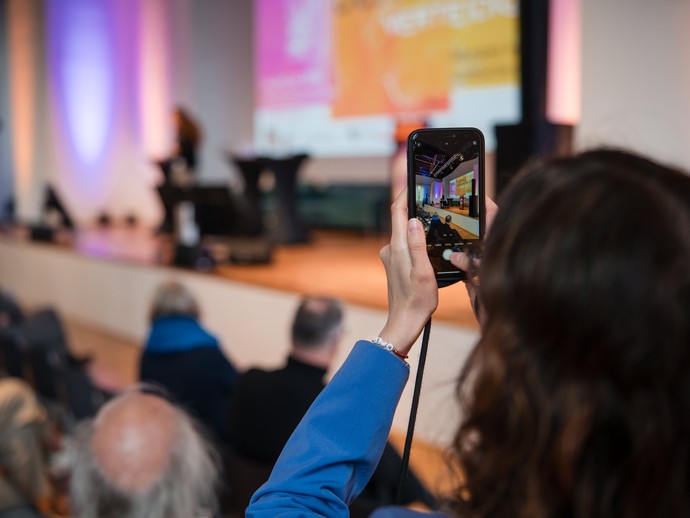 Foto eines Smartphones mit dem gerade ein Foto von der Bühne gemacht wird. (vergrößerte Bildansicht wird geöffnet)