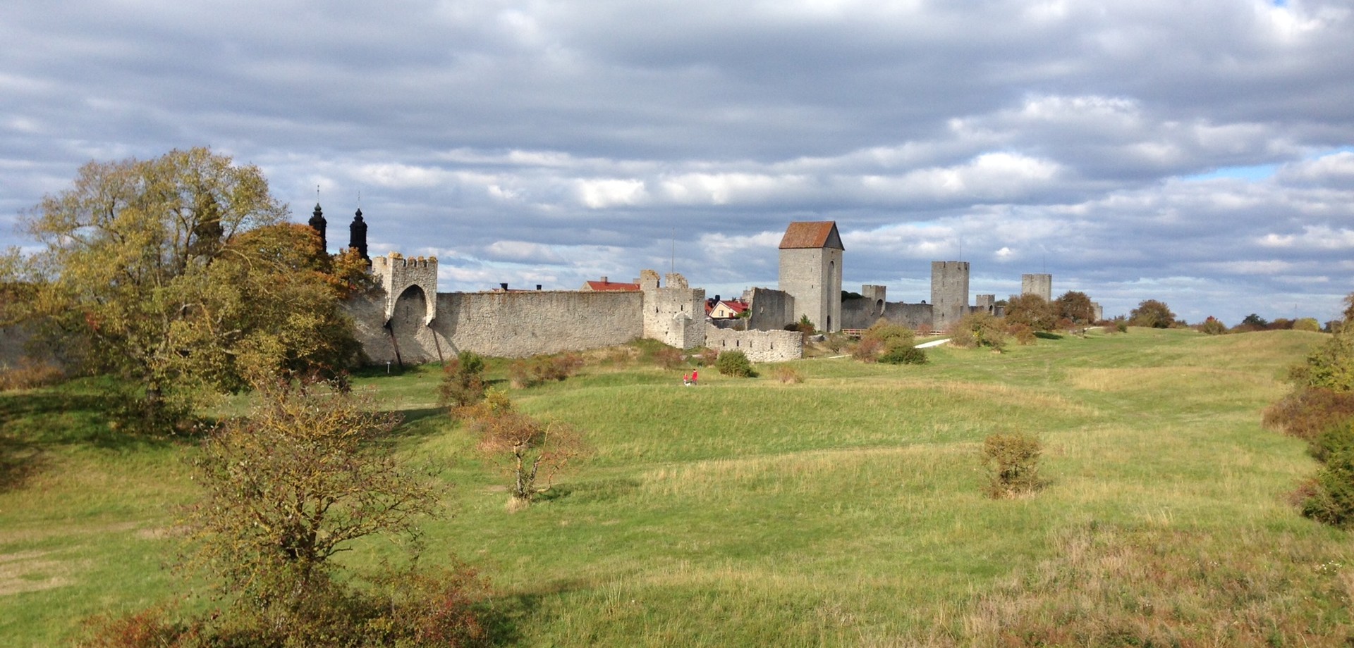 Stadtmauer von Visby/Gotland.Im Vordergrund eine grüne Wiese mit einigen Sträuchern. Der Himmel ist wolkenbedeckt