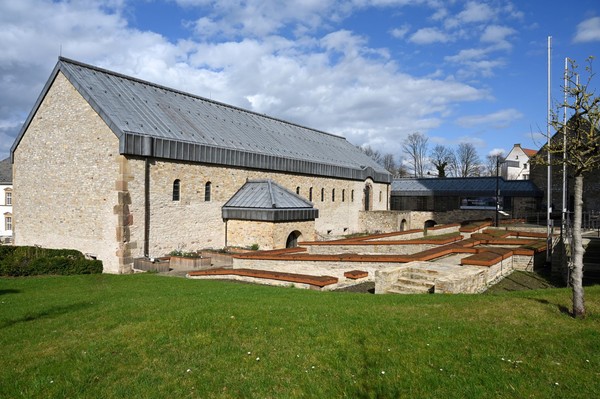 Gebäude mit steinernen Wänden und grauem Satteldach vor blauem Himmel und grünem Rasen