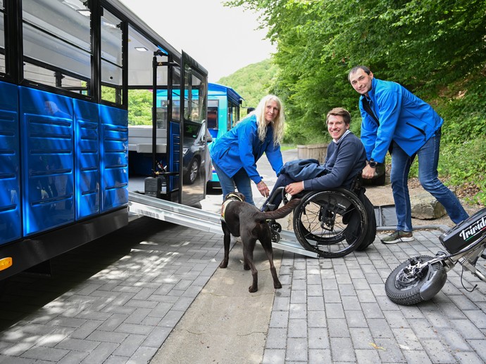 Zwei Mitarbeitende helfen einem Besucher im Rollstuhl und mit Assistenzhund über die Rampe in die Museumsbahn. Zwei Mitarbeitende helfen einem Besucher im Rollstuhl und mit Assistenzhund über die Rampe in die Museumsbahn.