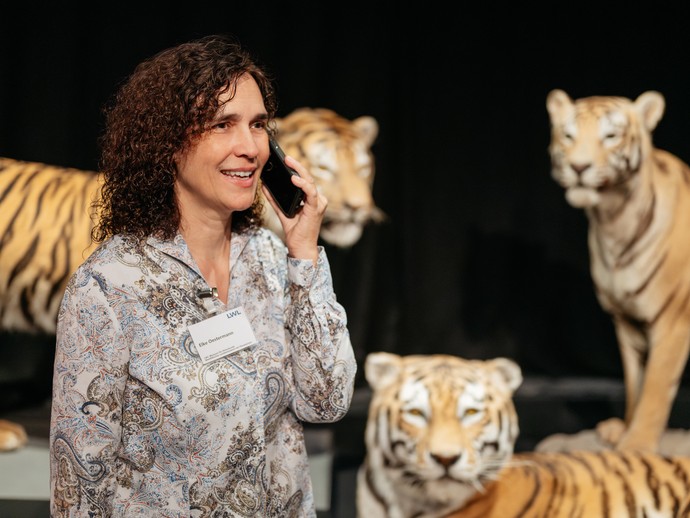 Eine Frau telefoniert neben drei präparierten Tigern.