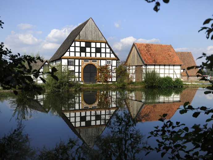 Zwei Häuser im LWL-Freilichtmuseum Detmold, die sich im Wasser spiegeln.