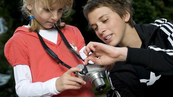 Eine junge Frau erklärt einem kleinen Mädchen eine Fotokamera