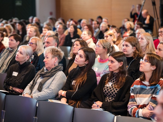 Foto von Teilnehmenden im Publikum die zuhören. (vergrößerte Bildansicht wird geöffnet)