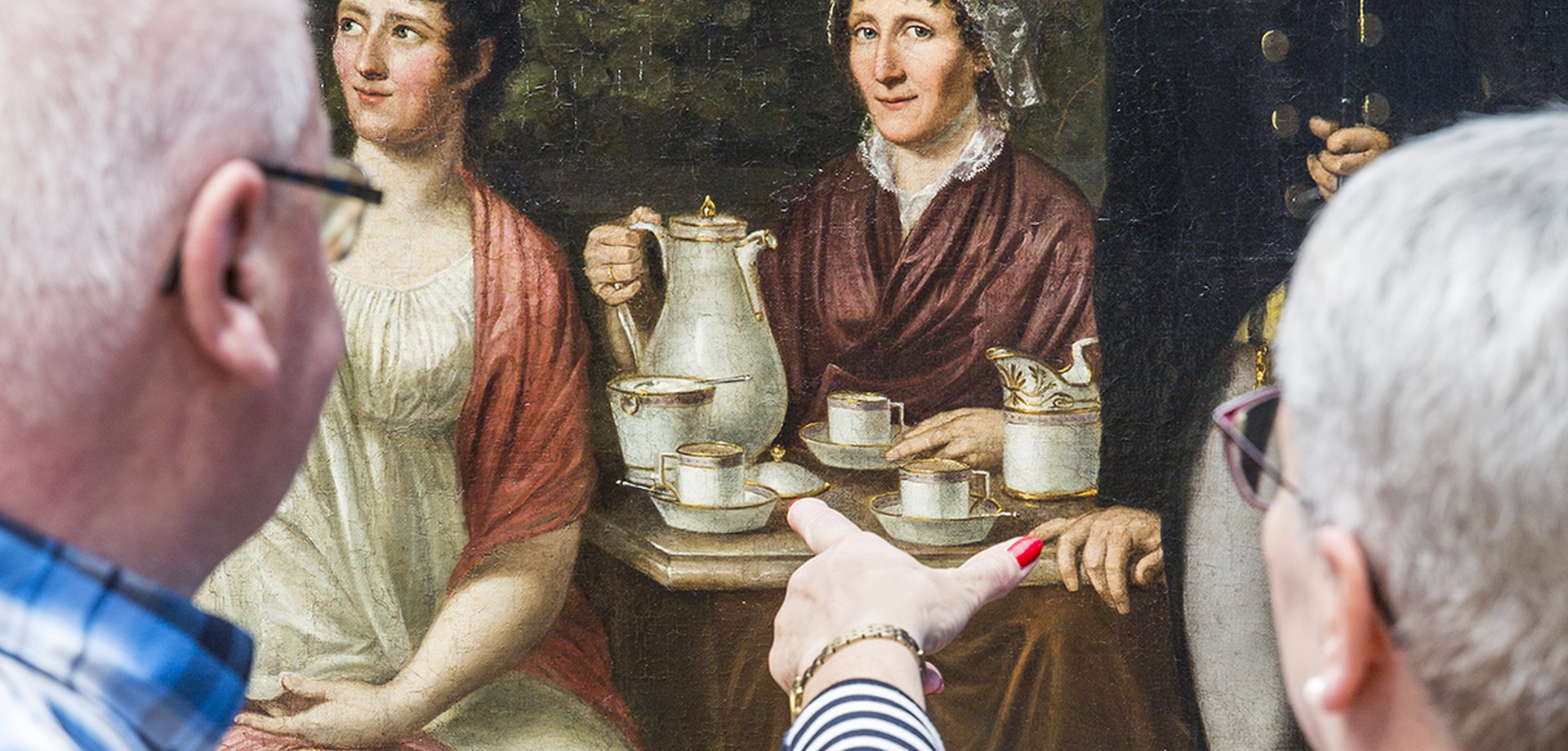 Zwei Menschen schauen sich ein Gemälde mit einem Familienportrait an.