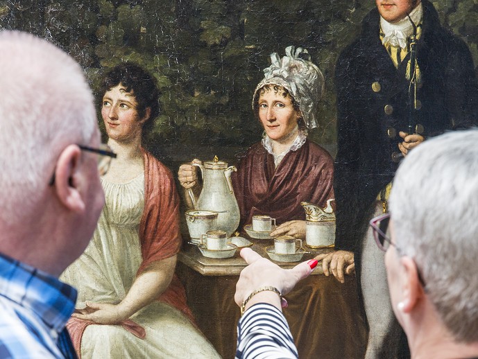 Zwei Menschen schauen sich ein Gemälde mit einem Familienportrait an.