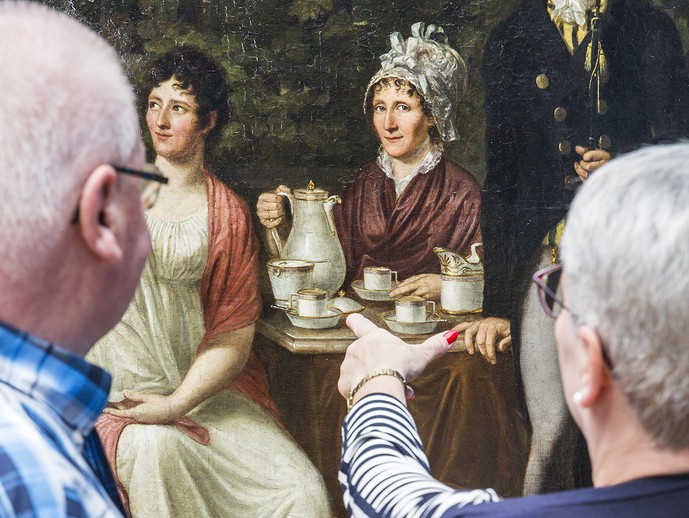 Zwei Menschen schauen sich ein Gemälde mit einem Familienportrait an.